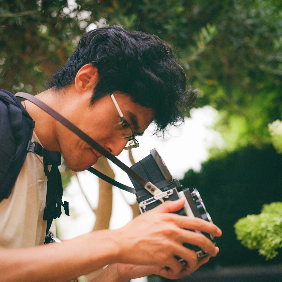 Henry Ren leaning over a medium-format camera, looking down into its viewfinder